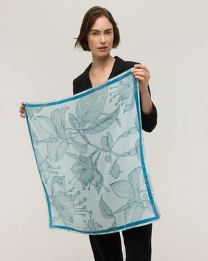 Foulard carré en soie et coton bleu ciel tenu déplié, montrant le motif floral dessiné au trait et la bordure bleu vif, Princesse & Dragon